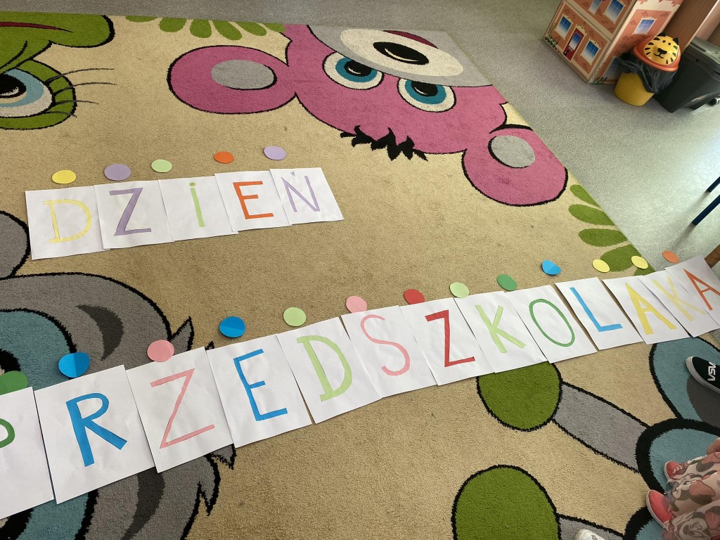Dzieci układają napis na dywanie z liter