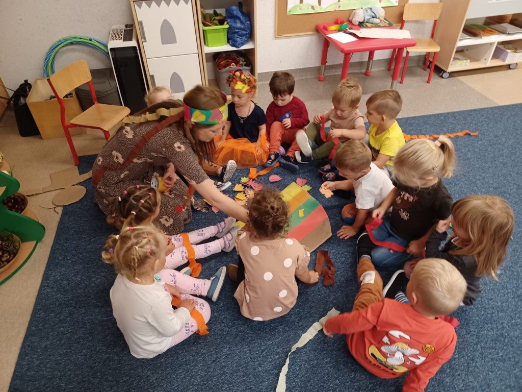 dzieci siedza na dywanie i przyklejaja kolorowe liscie
