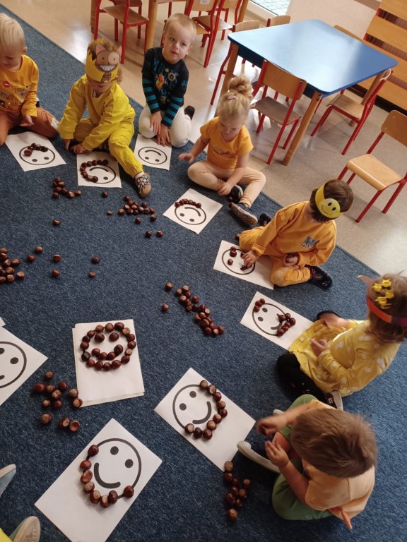 Dzieci siedza na dywanie u ukladaja usmiechy z kasztanow
