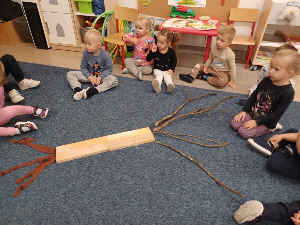 Dzieci siedza na dywanie i wspolnie tworza drzewo