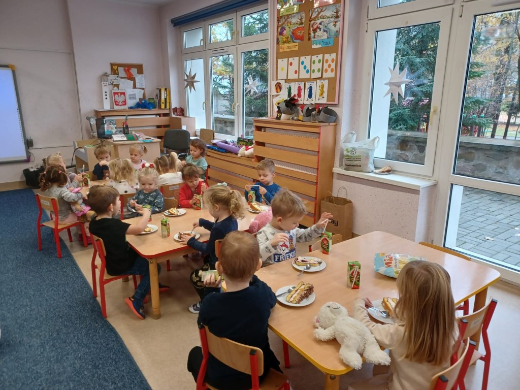 Dzieci siedza przy stolikach i jedza tort z okazji dnia misia
