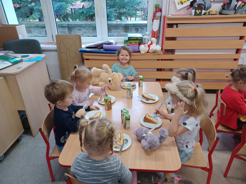 Dzieci siedza przy stoliku i jedza tort z okazji urodzin pluszowego misia