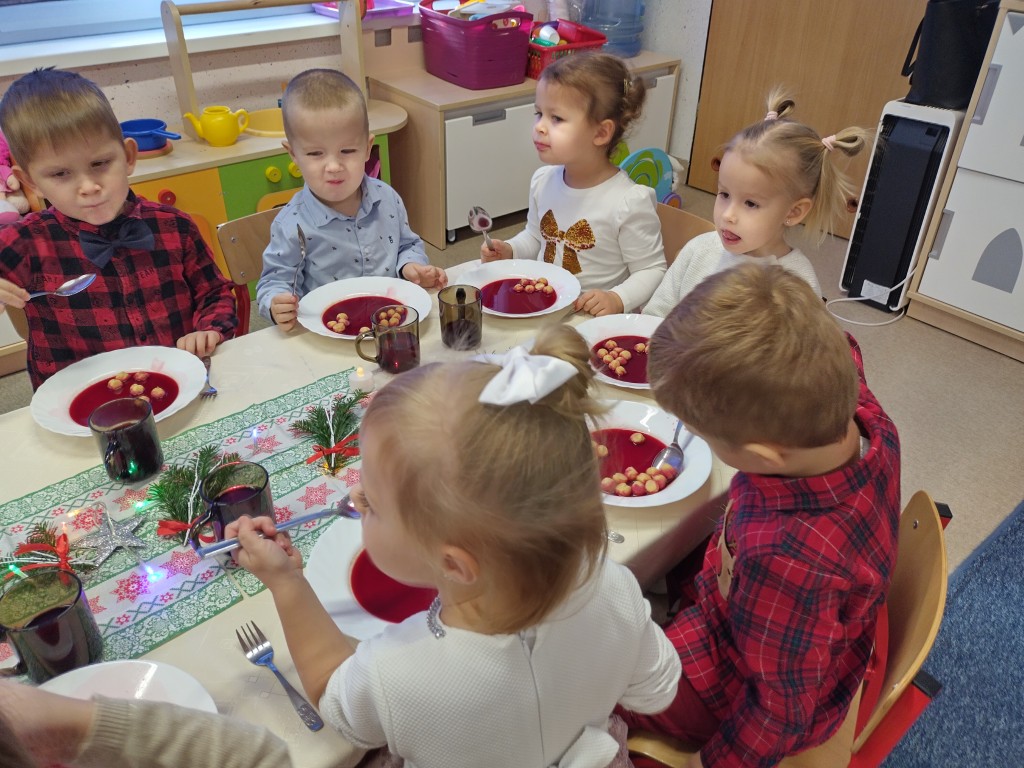 Dzieci siedza przy stolikach i jedza barszcz z okazji przedszkolnej wigilijki