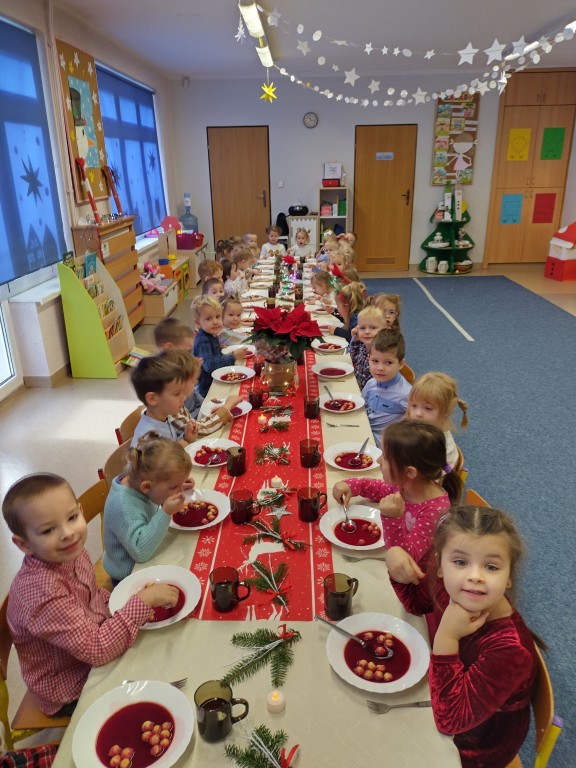 Dzieci z przedszkola siedza przy wigilijnym stole i jedza barszcz