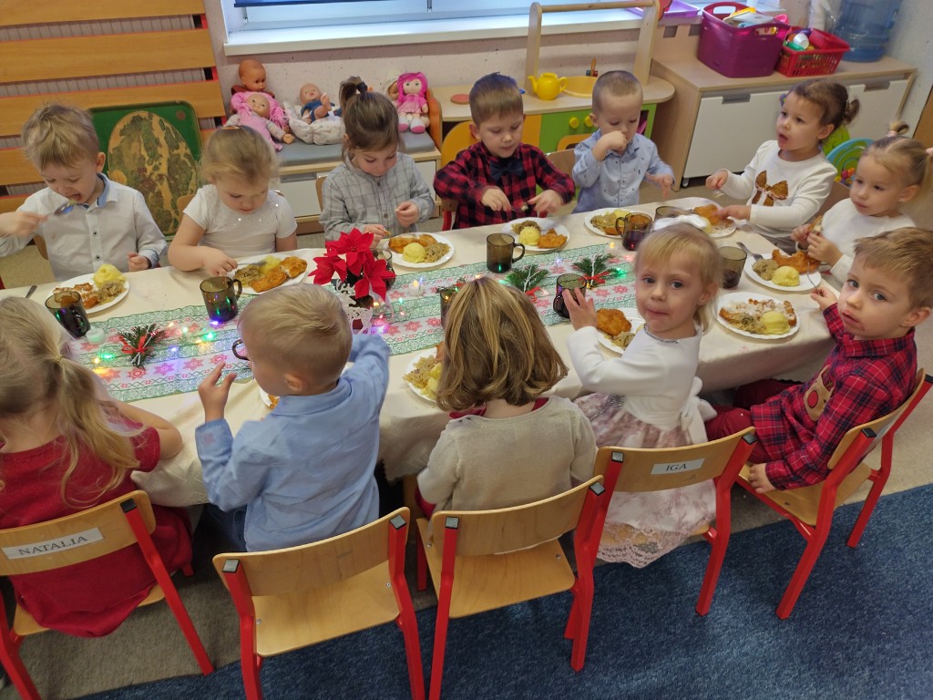 Dzieci siedza przy stole i jedza rybe z okazji wigilijki