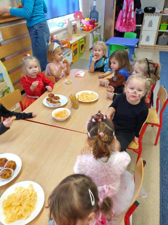 Dzieci przebrane w stroje karnawalowe jedza poczestunek przy stolikach