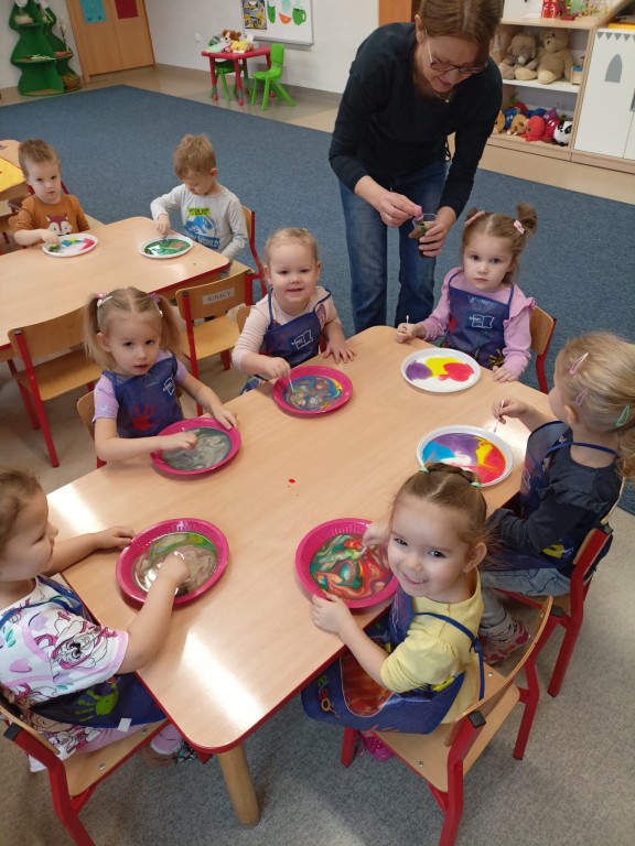 dzieci siedza przy stolikach i mieszaja kolory farb