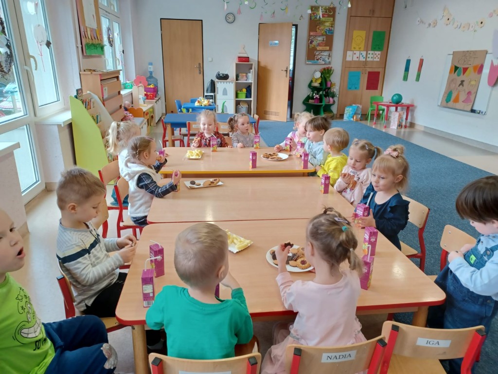 Dzieci siedza przy stolikach i jedza smakolyki z okazji dnia kobiet