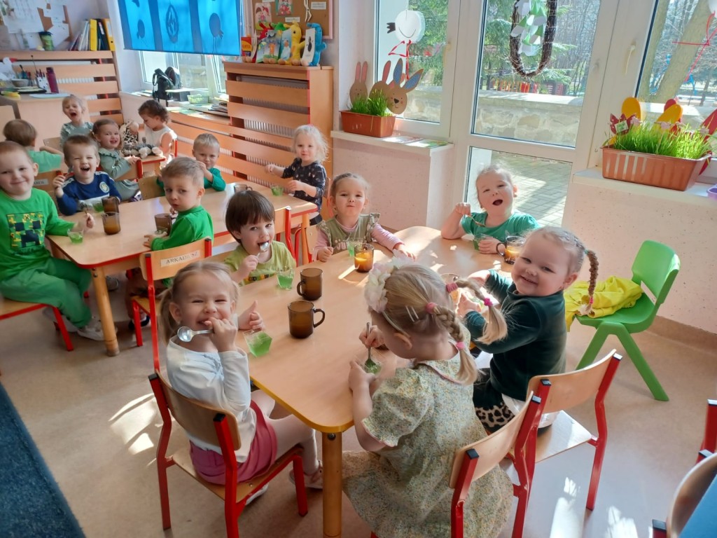 dzieci siedza przy stolikach i jedza zielone galaretki