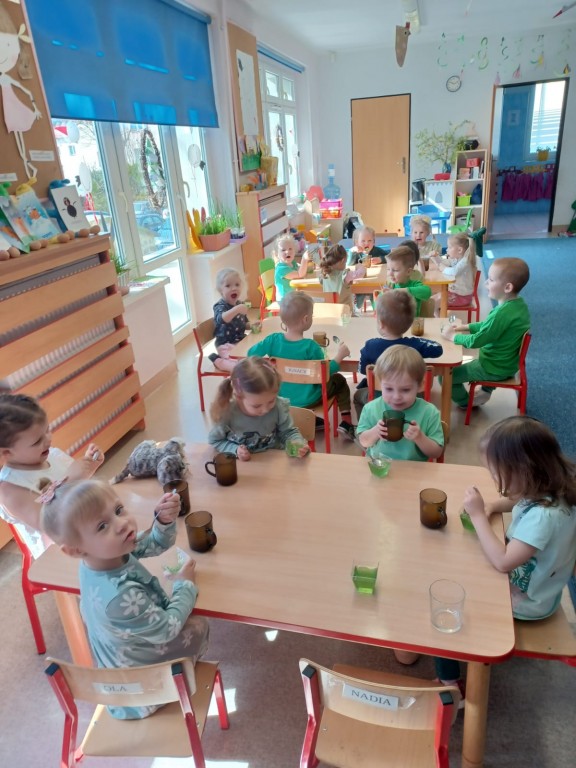 dzieci siedza przy stolikach i jedza zielone galaretki z okazji pierwszego dnia wiosny