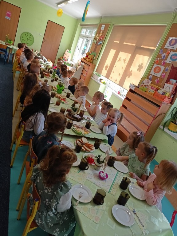 dzieci siedza przy stolikach i jedza sniadanie wielkanocne