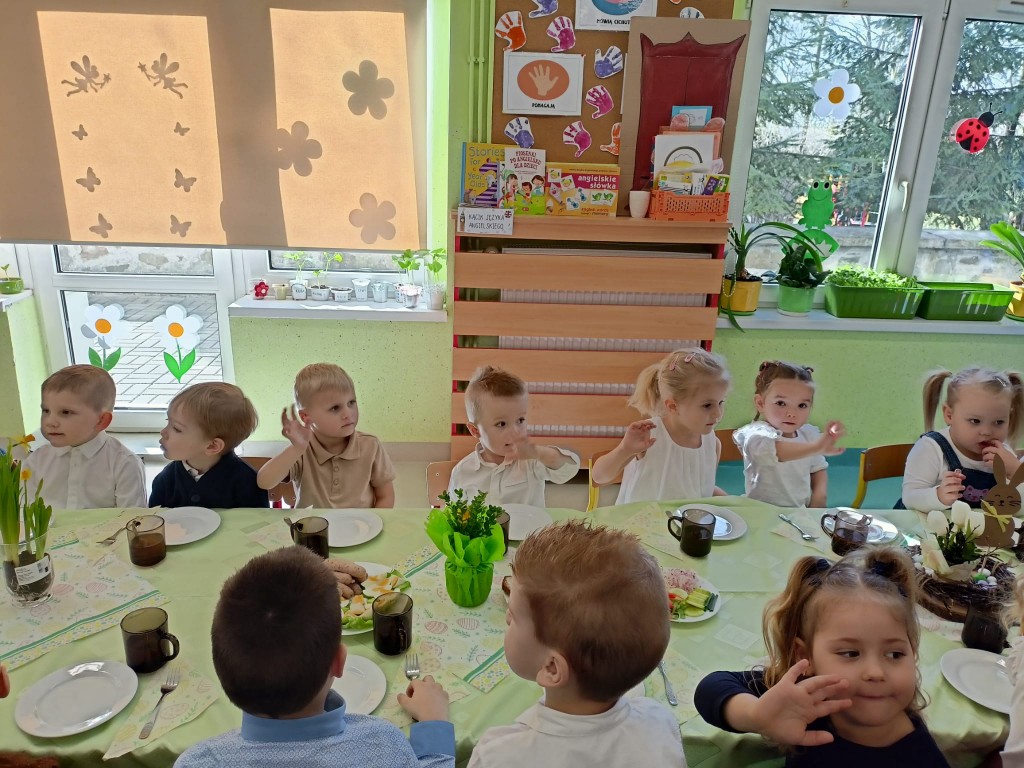 dzieci siedza przy stolikach i jedza sniadanie wielkanocne