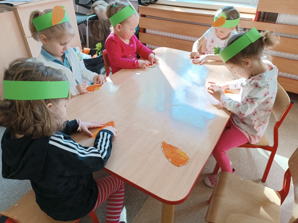 dzieci siedza przy stoliku i wylepiaja plastelina papierowa marchewke