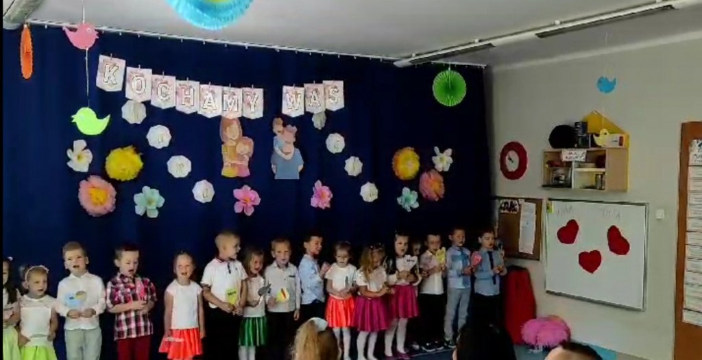 Dzieci stoją w rzędzie, w ręku trzymają serca i śpiewają piosenkę