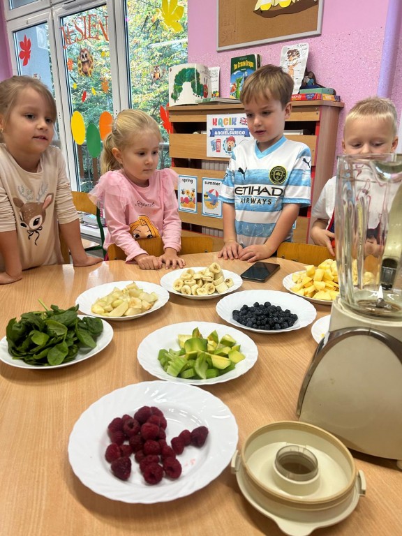 Dzieci stoją przy stole wypełnionym talerzami z owocami